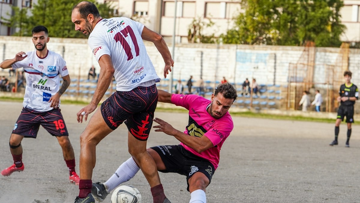 Soccer players competing for the ball on a dirt field